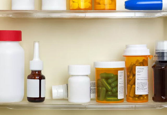 Several containers of over the counter and prescription medications on the shelves of a medicine cabinet.