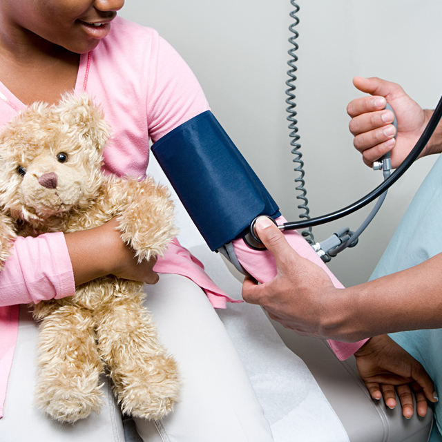 Child holding a teddy bear while a doctor checks her blood pressure