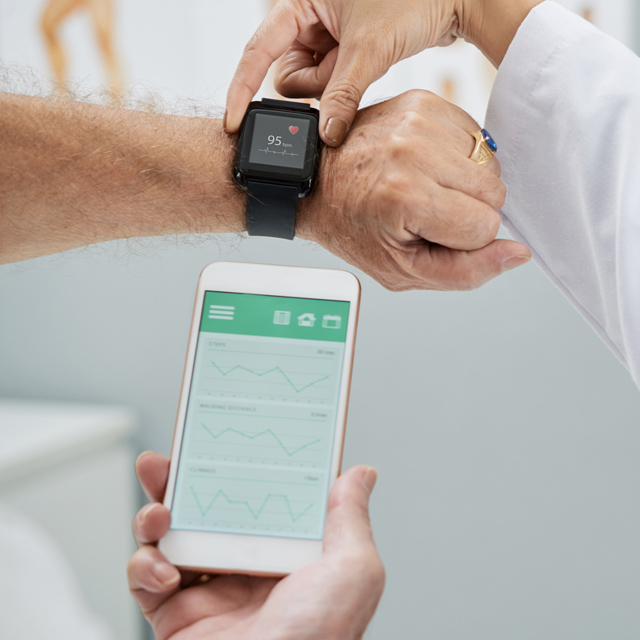 Image shows a wrist with a smart watch and a hand holding a phone indicating heart rate.