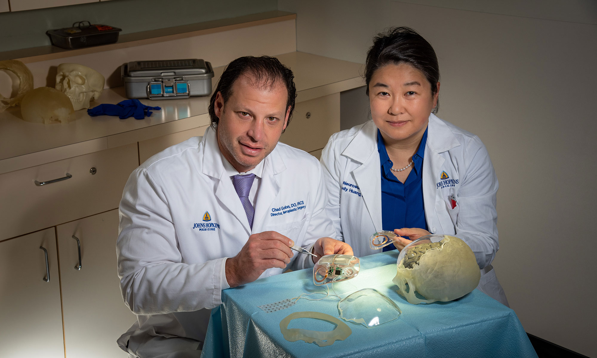 Craniofacial plastic surgeon Chad Gordon and neurosurgeon Judy Huang, wearing lab coats, hold neuroplastic devices in their hands that consist of clear plastic implants with electric parts embedded in them.