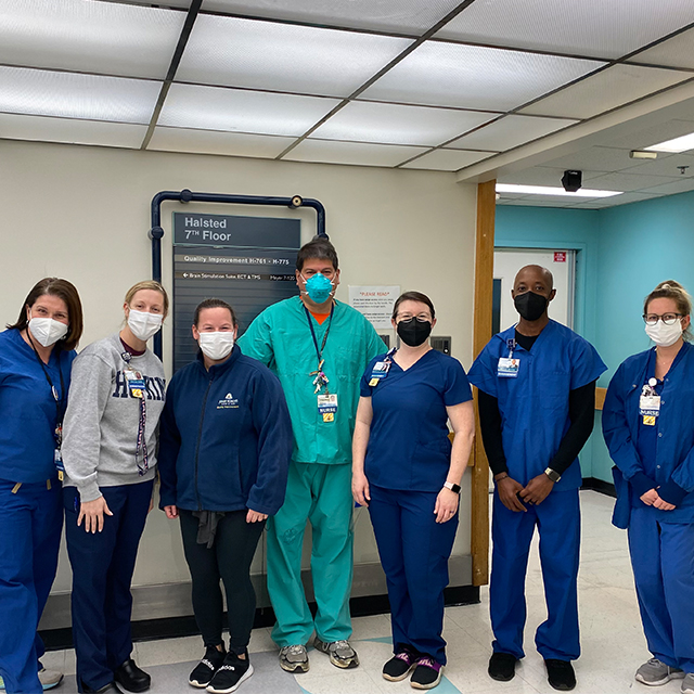 Seven members of the Quality Improvement team pose for a photo on the 7th floor of the Halsted building. All are wearing scrubs and masks.