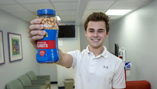A teenage boy holding a jar of peanuts and smiling