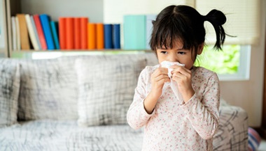 A little girl wipes her nose with a tissue.