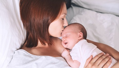 New mother kissing her newborn baby on the head