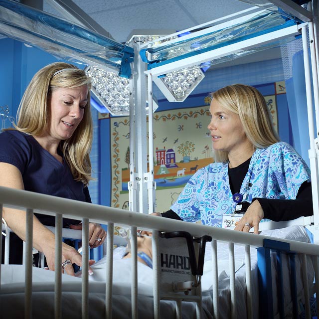 two nurses leaning over infant in hospital bed