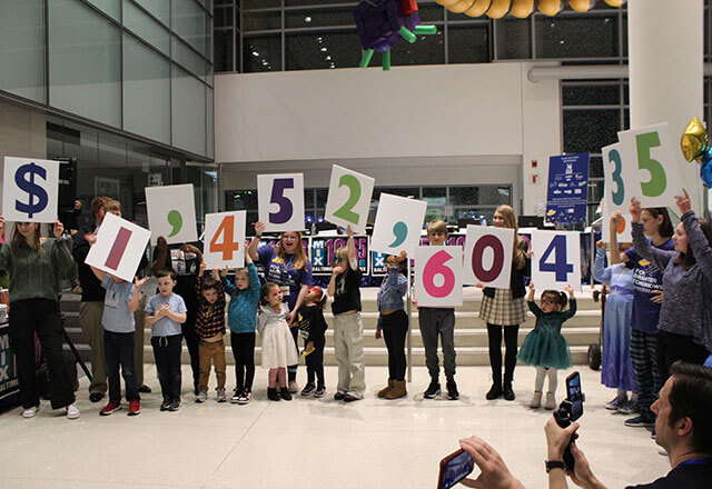 A group of people holding cards with numbers on them spelling out 1,453,157.35