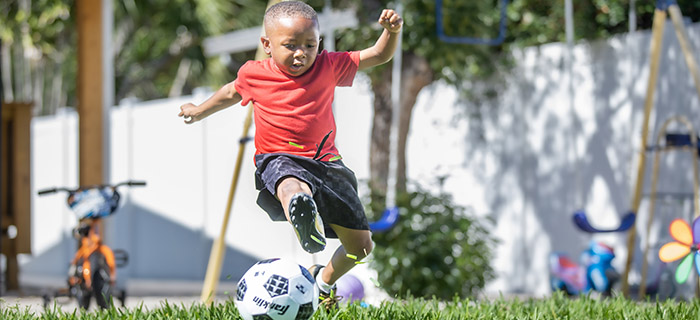 Young boy kicking a soccer ball in his back yard. 