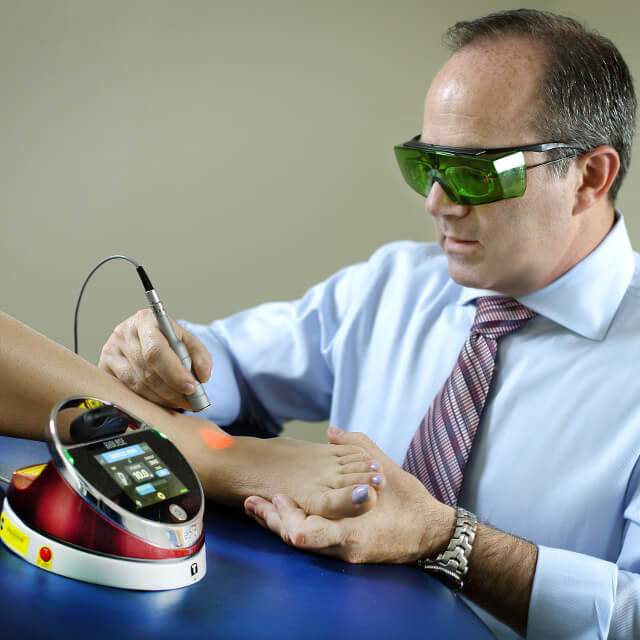 Therapist using a laser therapy device on a patient's ankle.