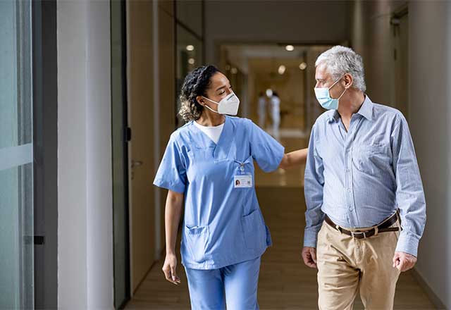 Healthcare provider walking with a patient down a hospital hallway.