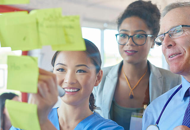 Two clinicians watch as a third writes on a post-it