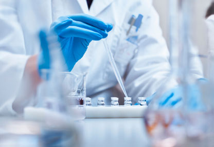 Researcher in white coat and blue gloves filling a vial