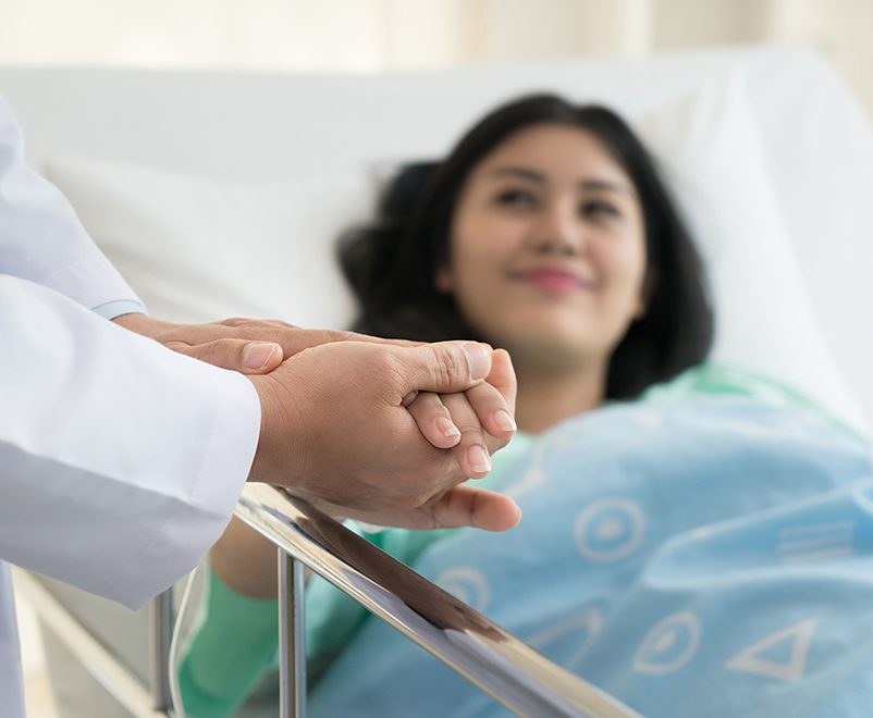doctor holds hand of patient in hospital bed