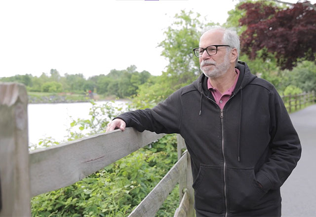 Bob leans against a fence next to a small lake
