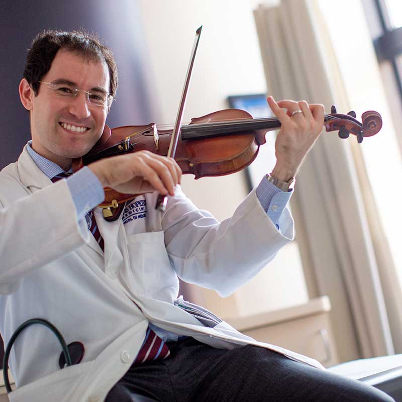 Dr. Alex Pantelyat sitting on a chair and playing a violin
