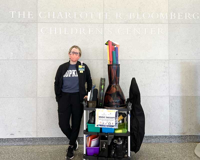 A Johns Hopkins music therapist standing next to a cart full of music therapy instruments.