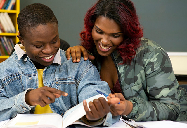 A female presenting and male presenting couple read a book together.