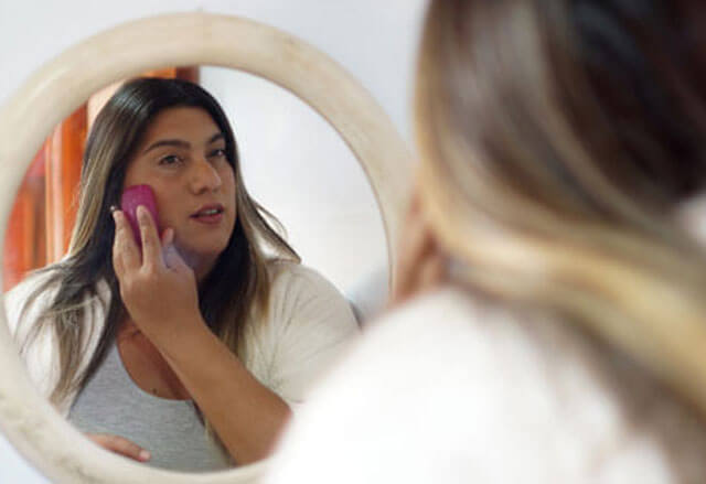 Woman looks into mirror while applying makeup.