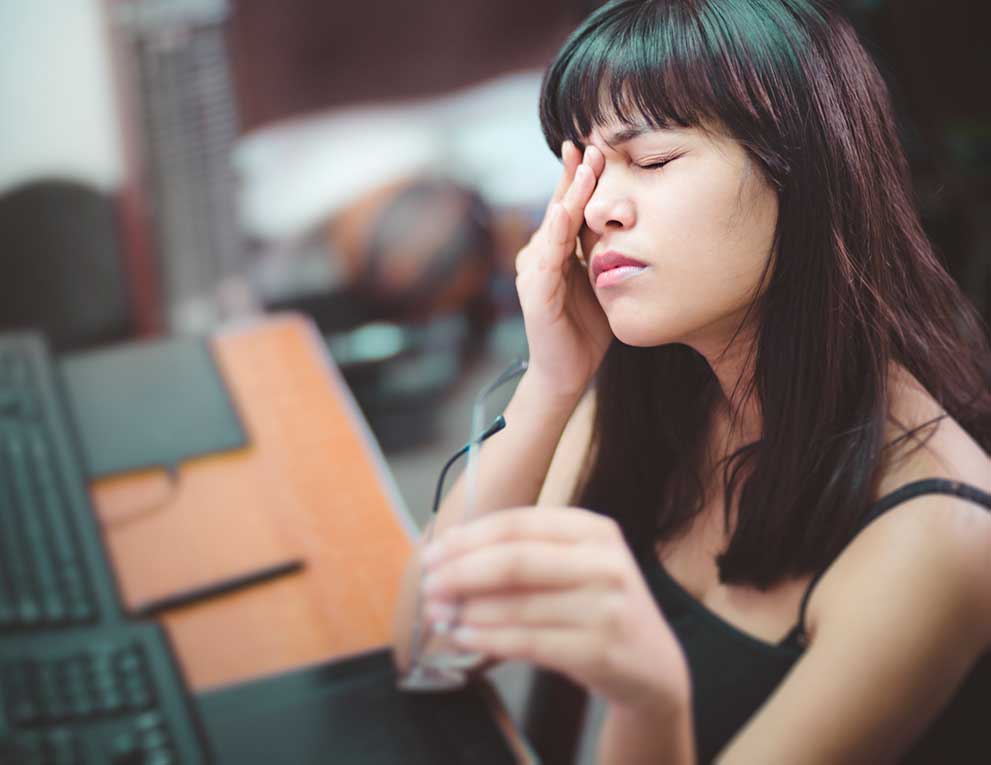 Woman sitting at a desk rubs her right eye in discomfort.