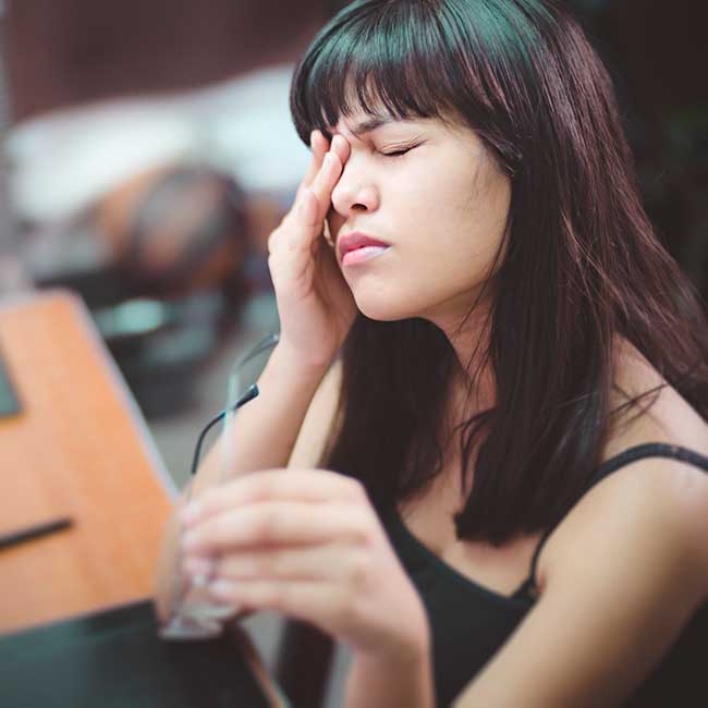 Woman sitting at a desk rubs her right eye in discomfort.