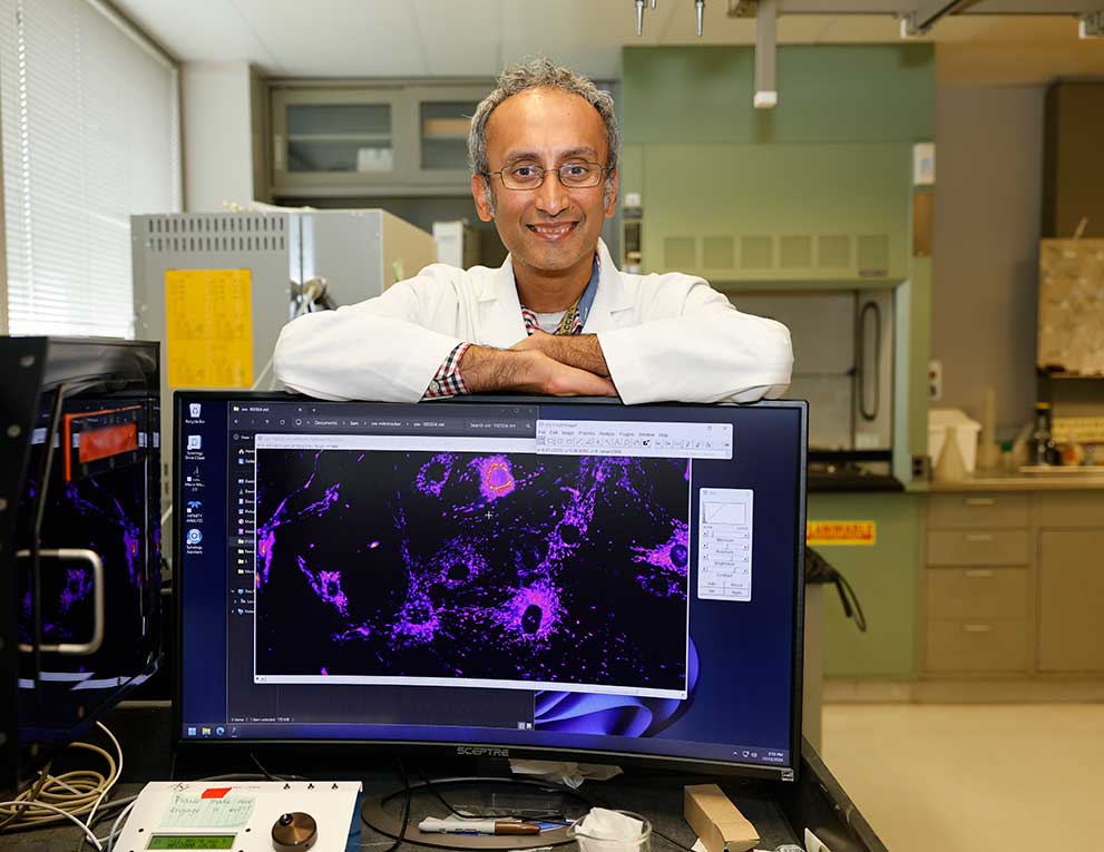 Dr. Suresh smiling with his arms resting across a wide computer monitor