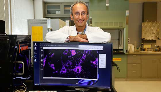 Dr. Suresh smiling with his arms resting across a wide computer monitor