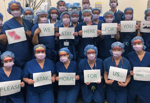 Johns Hopkins Outpatient Center staff holding signs reading "We stay here for you, please stay home for us"
