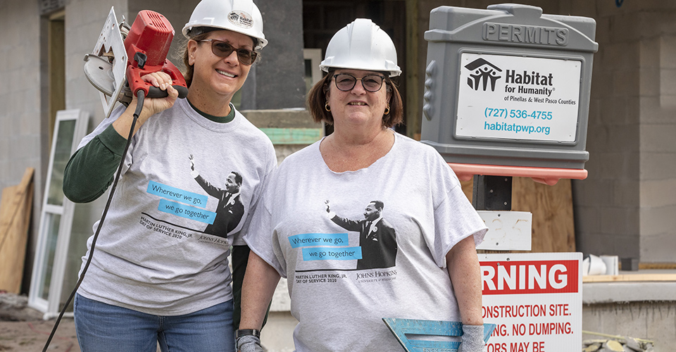 Two woman stand together outside of a construction site.