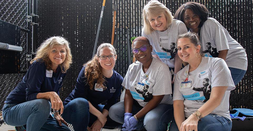 A group of smiling volunteers pose together while working outside.