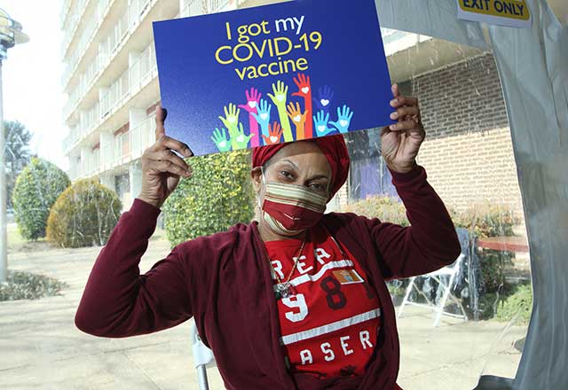 a black woman holding a sign saying she's been vaccinated against COVID-19