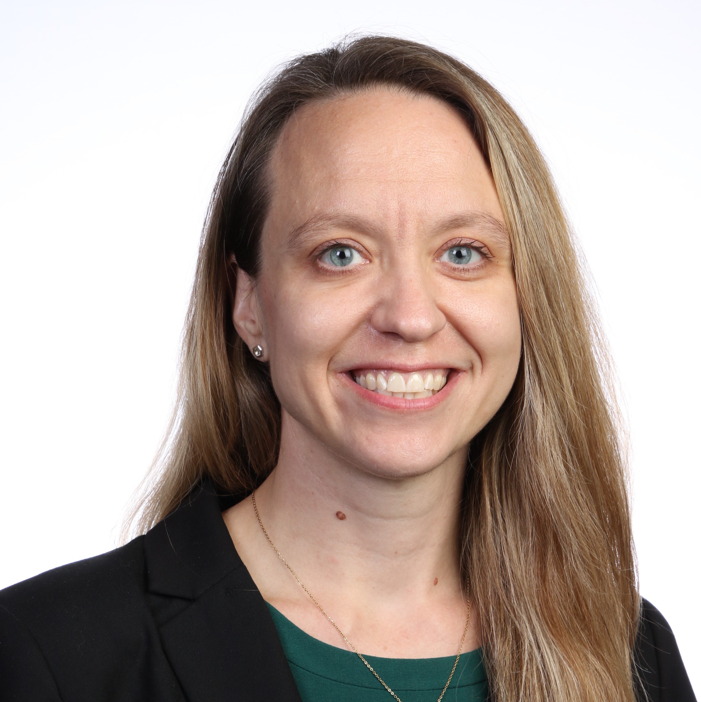 Theresa Boyer smiles for a professional headshot in front of white background while wearing green top and black blazer.