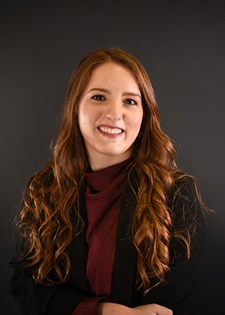 Paola Pena smiles for a professional headshot in front of a dark background
