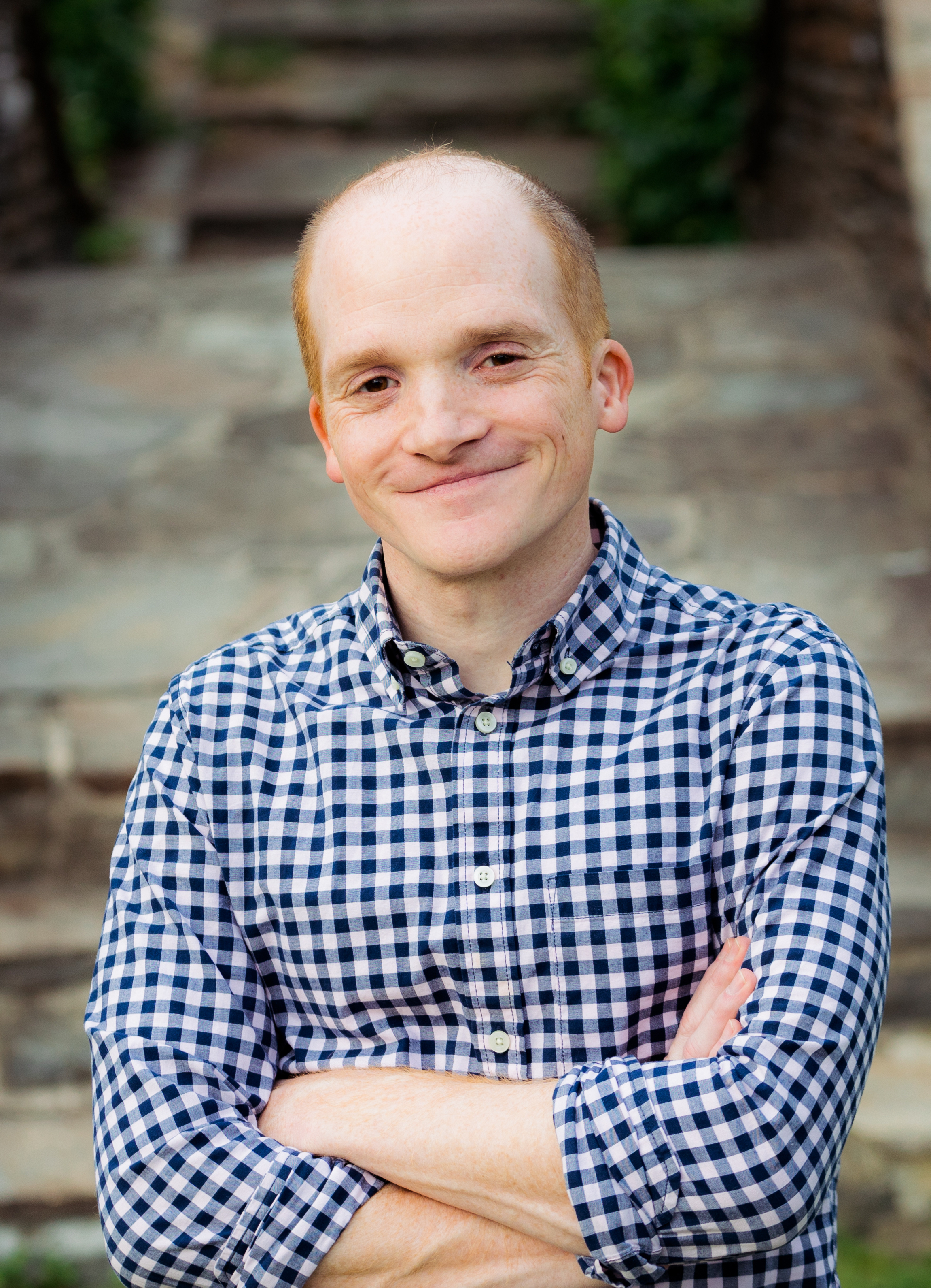 Nathan Gray, wearing a blue and white gingham shirt, smiles for a photo with his arms crossed.
