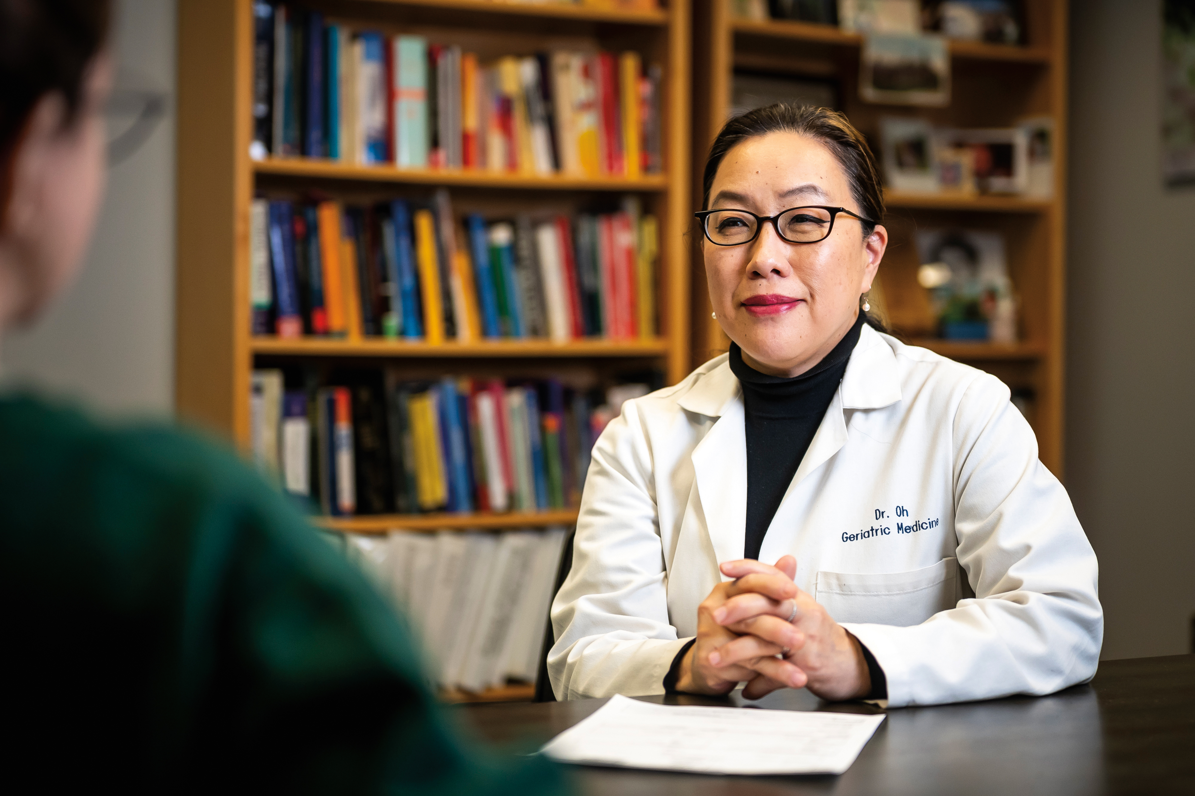 Dr. Esther Oh sitting at a table with hands folded