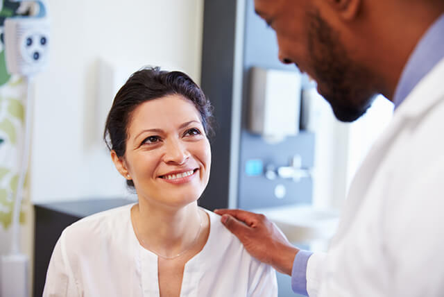 Female patient smiling up at doctor who is talking while touching her shoulder.