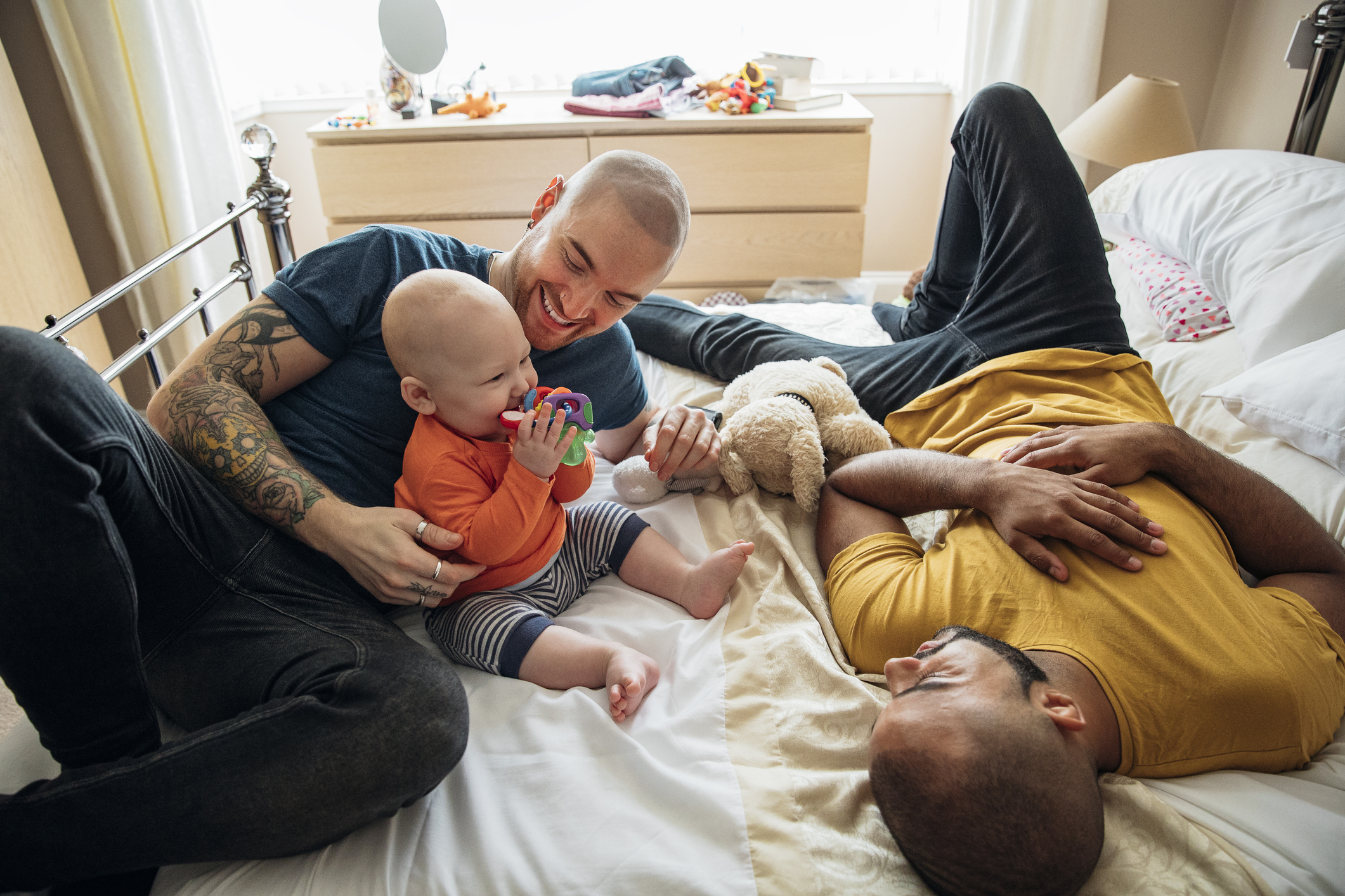 Interracial gay male couple playing with son in bed
