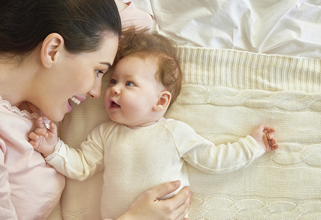 single parent families - woman smiling with baby in bed