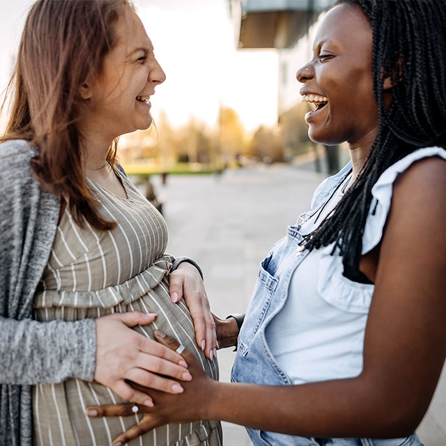 two women laughing as one touches pregnant friends belly