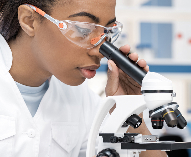 woman wearing goggles looking into microscope