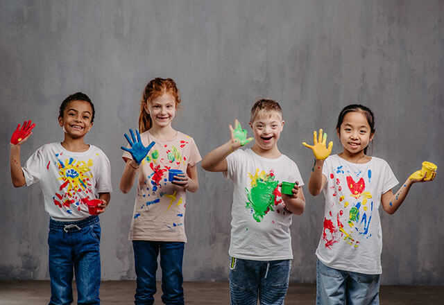 four children with finger paints and wearing tee-shirts with paint on them 