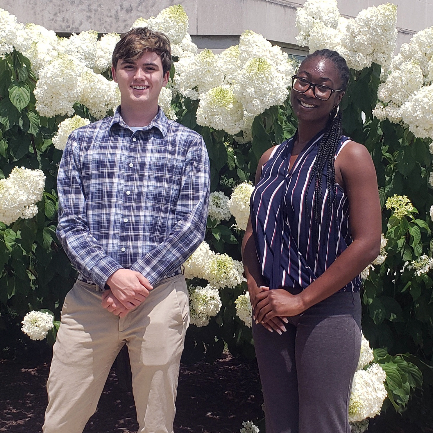 Two SHARP students outside in front of flowering bushes