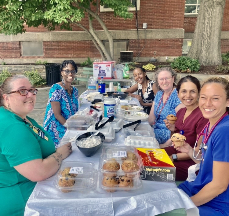 Hospitalists enjoying a picnic together outside around a long table.