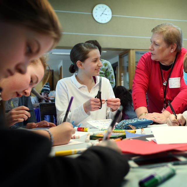 A group of girls making cards, with a woman talking to one of the girls.