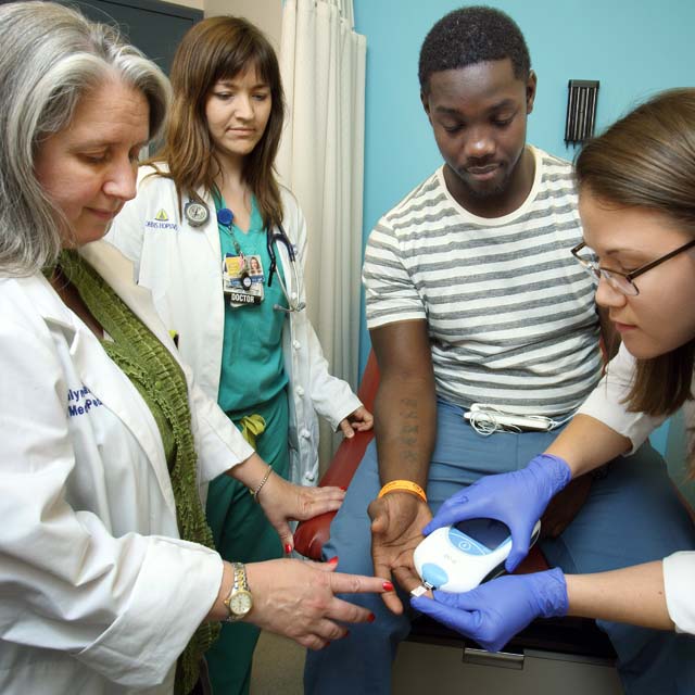 Photo shows pharmacist Amanda Sowell checking Deron Bridges’ blood-thinninglevel, as After-Care Clinic co-director Rosalyn Stewart, far left,and emergency medicine physician Anneliese Cuttle look on