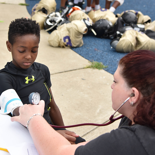 Johns Hopkins Hospital nurse practitioner Suzette Heptinstall checks 7-year-old football player Elijah Stanley’s blood pressure during a physical exam.