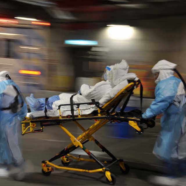 Photo of an Ebola drill in progress with mock patient on a gurney being escorted by health care workers in protective suits.