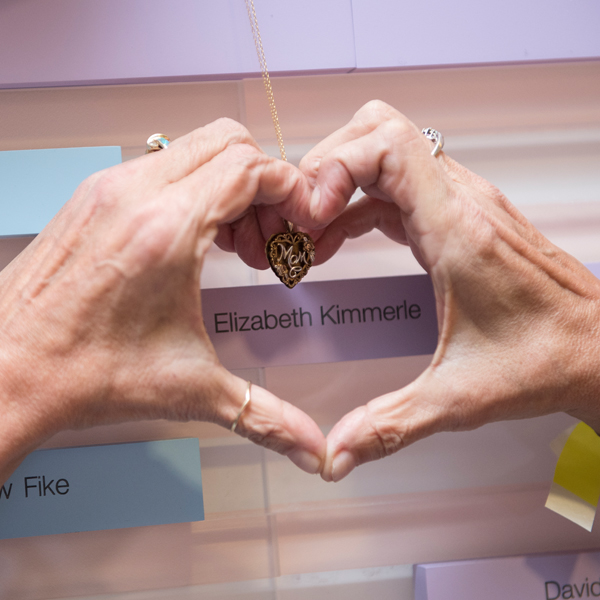 Hands in the shape of a heart around a name on the organ donation wall