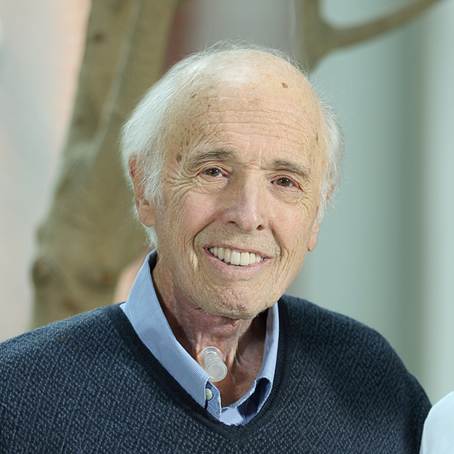 Patient Al Friendly Jr. looking into camera and smiling. He has on a blue sweater and has whitish-gray hair. 