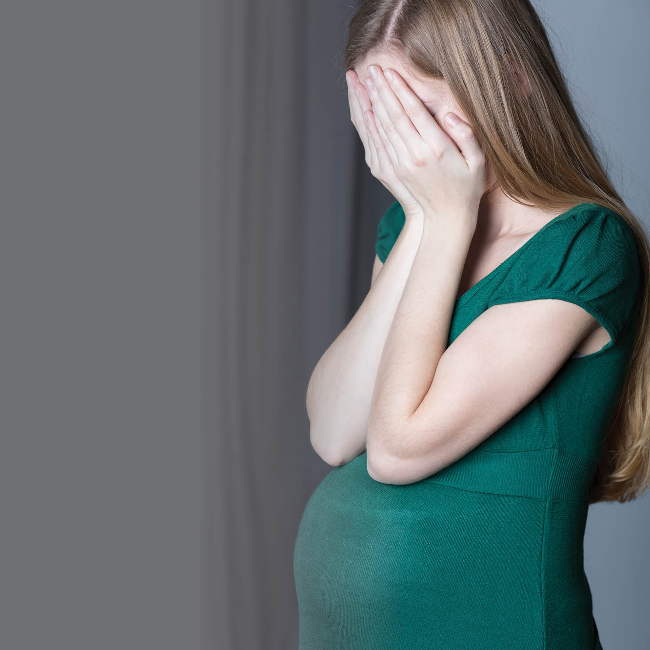 A photo shows a pregnant woman with her hands over her face. 