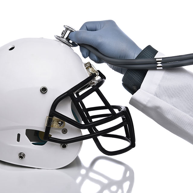 A doctor holding a stethoscope up to a white football helmet.