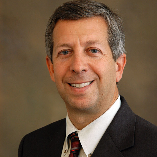 Andrew Satin wearing a dark suit with a white shirt and tie.
